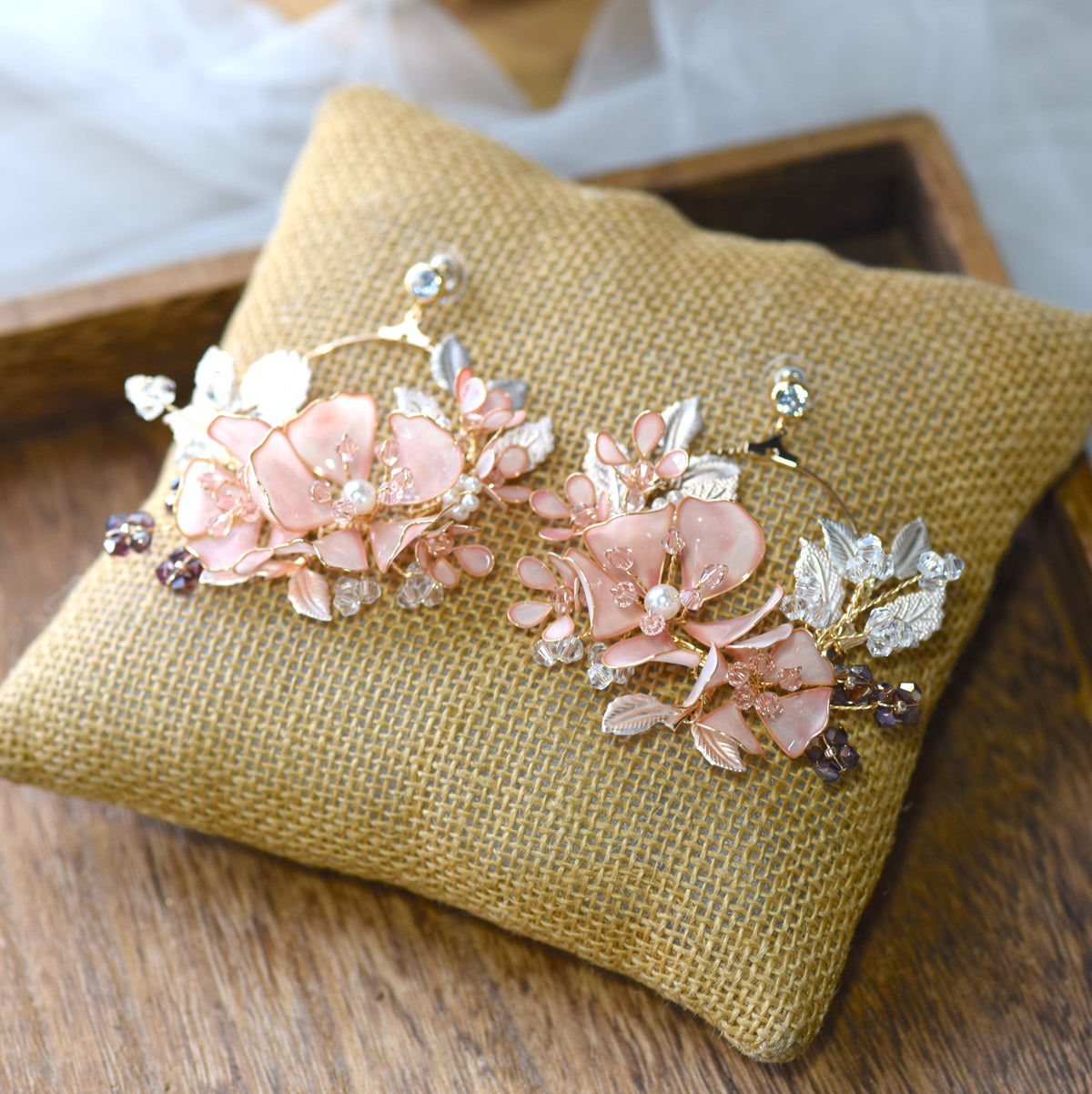 Eos blush pink resin floral earrings laid on a jute cushion