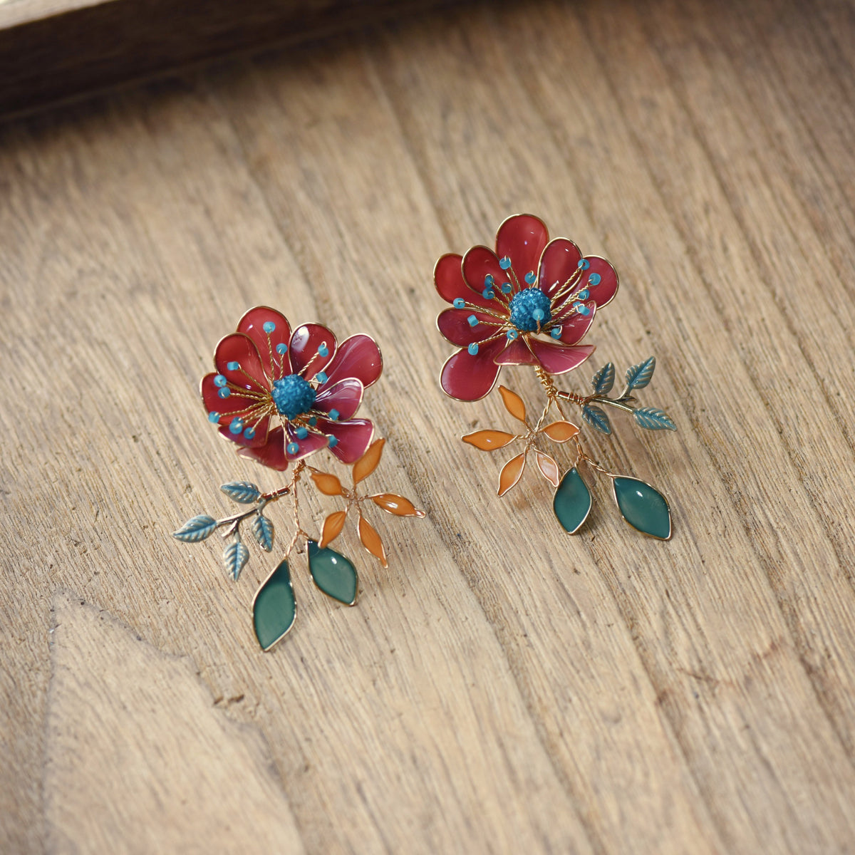 Isariah red resin floral stud earrings detail showing blue centre and orange accents