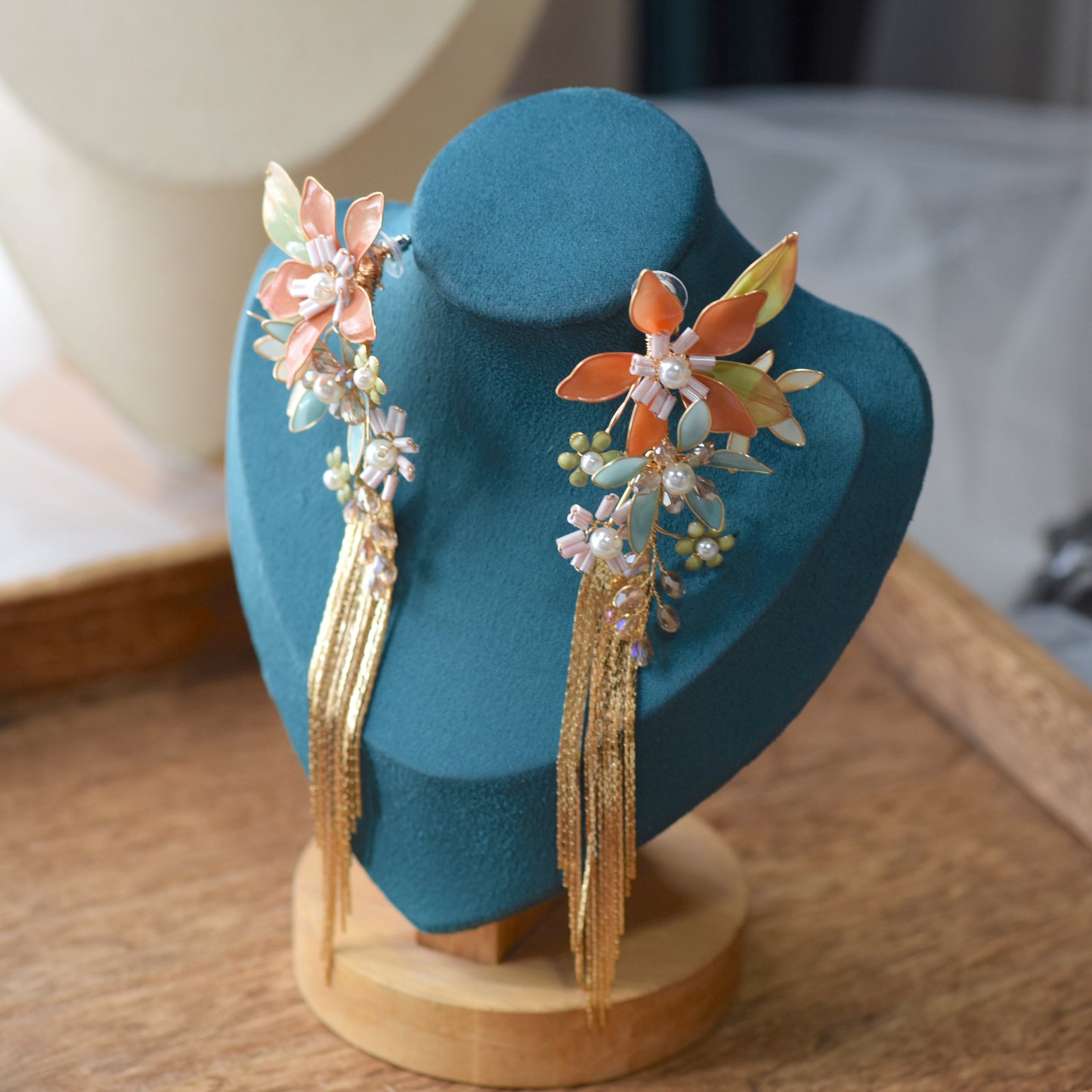 Jeanne coral mint and blue resin floral tassel earrings on a teal display stand