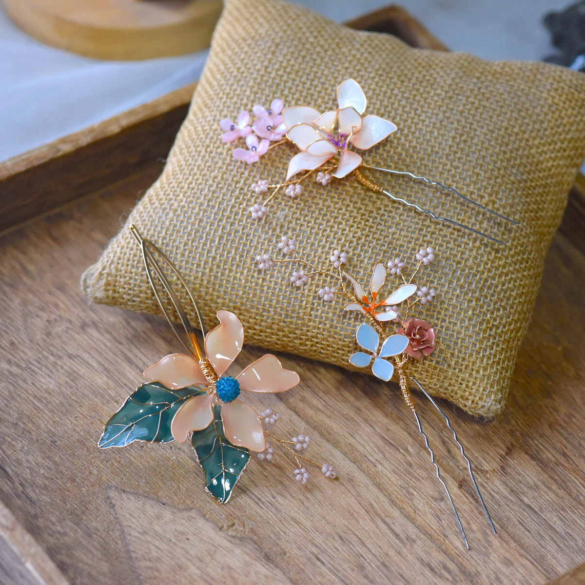 Micaela blush and ivory resin floral hair pins with sage leaves on a jute cushion