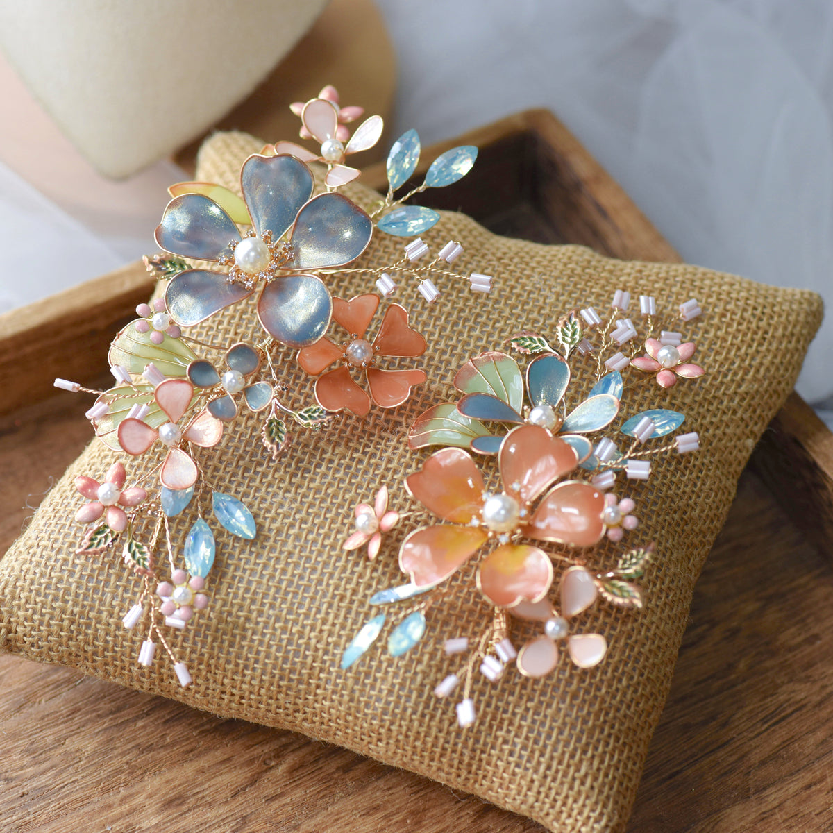 Reine set of two blush pink and dusty blue resin floral hair pins with pearl centres on a jute cushion