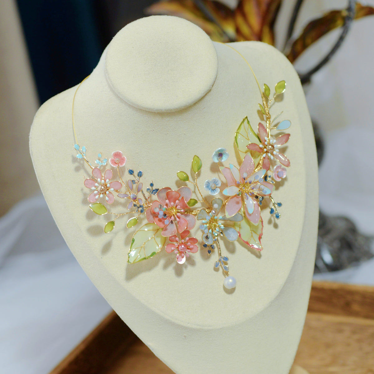 Trina coral and green floral statement necklace displayed on a stand showing the garland design