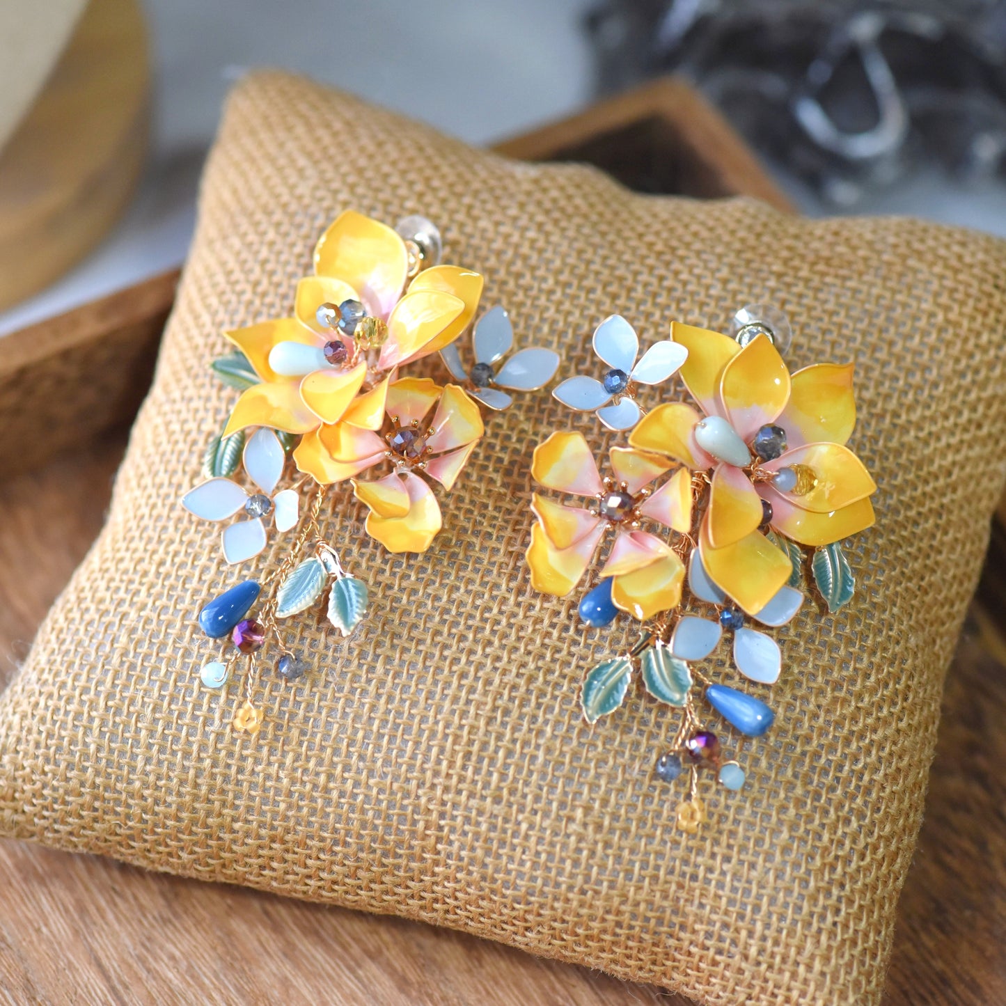 Amberglow amber yellow and peach resin floral earrings on jute cushion
