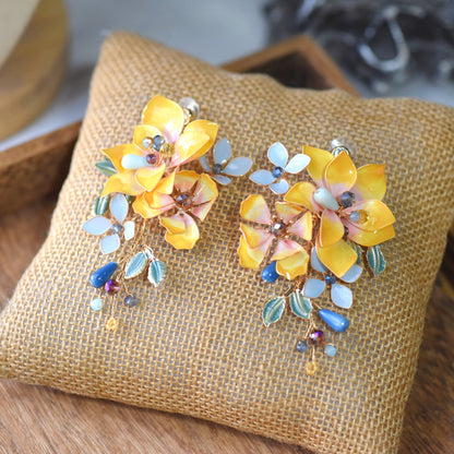 Amberglow amber yellow and peach resin floral earrings on jute cushion
