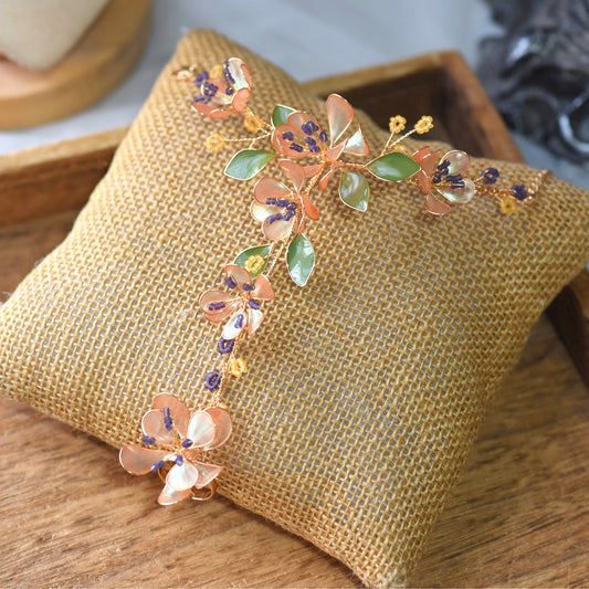 Apricot Fleur hand harness with apricot, lavender and green resin flowers on gold wire, displayed on a woven cushion