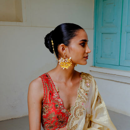 Model wearing Helios yellow resin floral earrings with hair harness, styled with a low bun and red outfit
