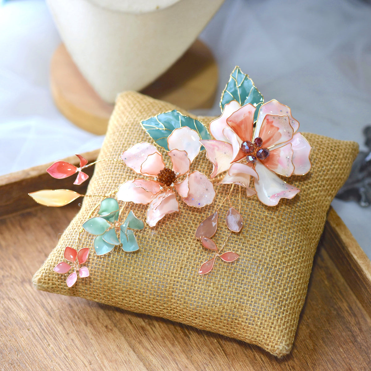 Aeris blush and coral resin floral bridal hair vine with seafoam leaves on jute cushion
