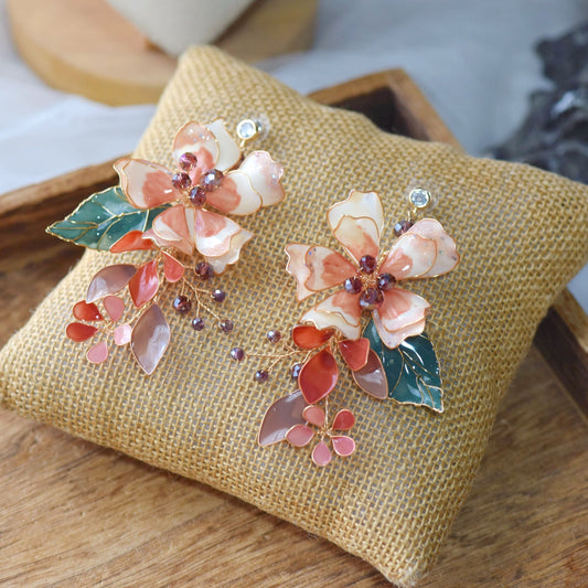 Aeris blush and coral resin floral earrings with gold-outlined petals on a jute cushion
