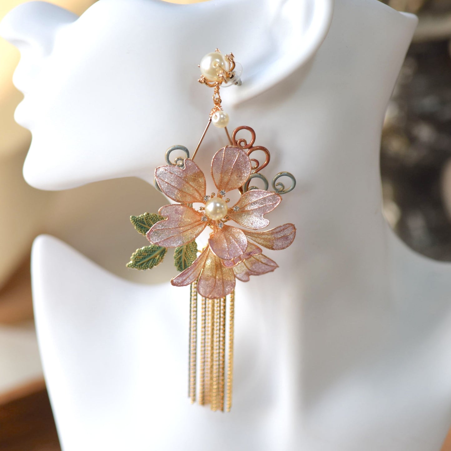 Amaris lavender and mauve resin floral earrings with pearl centres and golden chain tassels on a jute cushion
