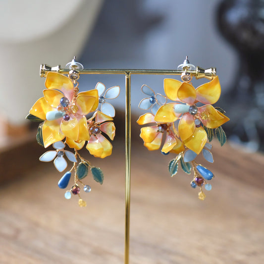 Amberglow amber yellow resin floral earrings with peach petals and enamel leaves on display stand

