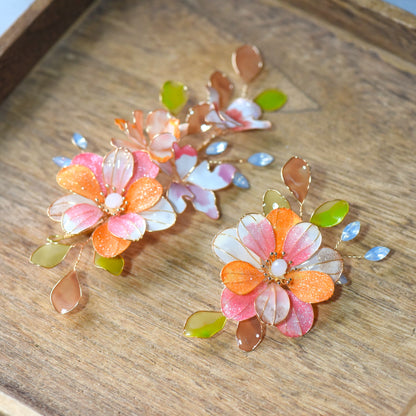 Close-up of Arancia hair accessory highlighting glossy coral resin petals, subtle shimmer and handcrafted gold finish
