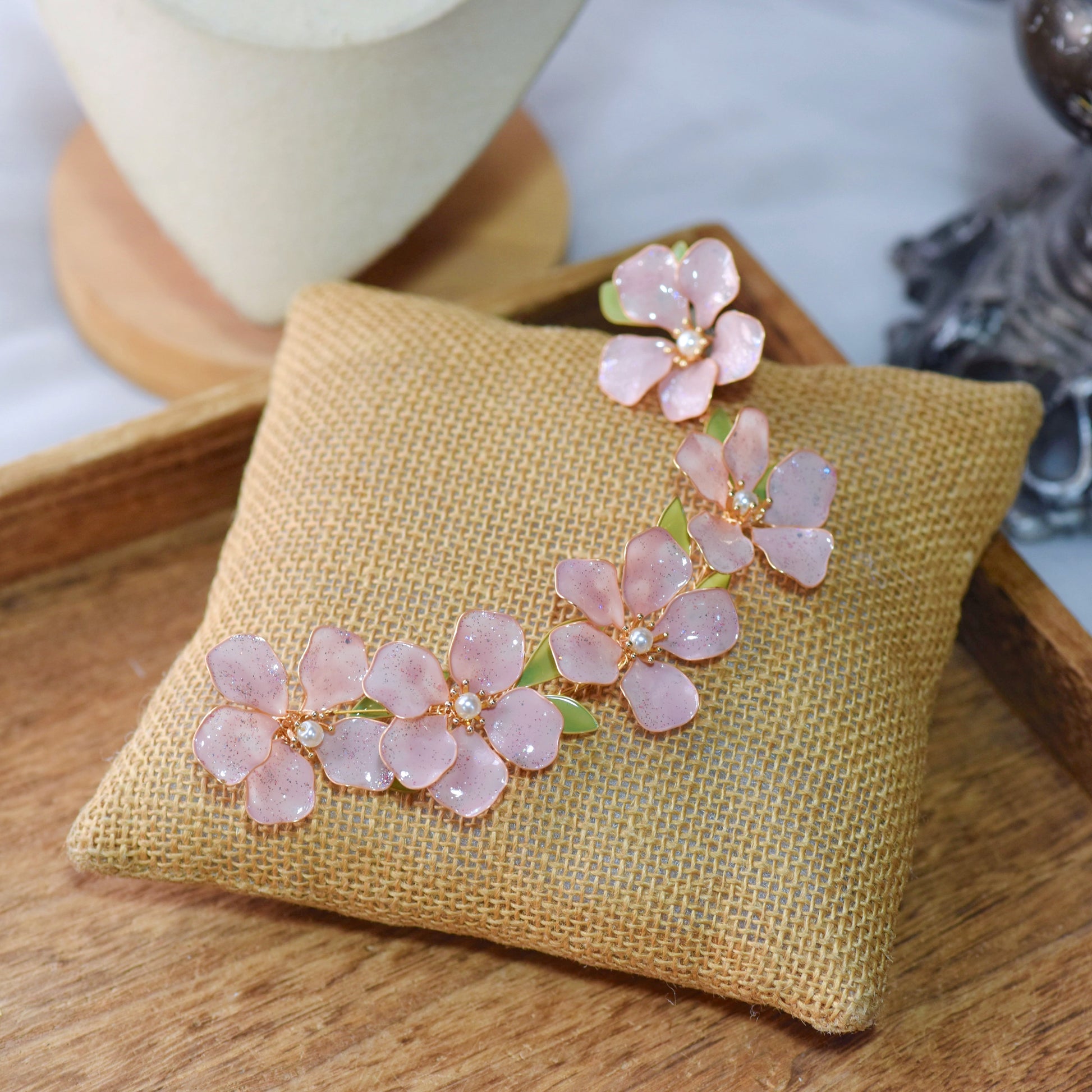 Aubri pink resin floral bridal earrings with hair harness displayed on jute cushion
