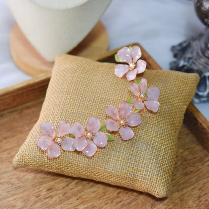 Aubri pink resin floral bridal earrings with hair harness displayed on jute cushion
