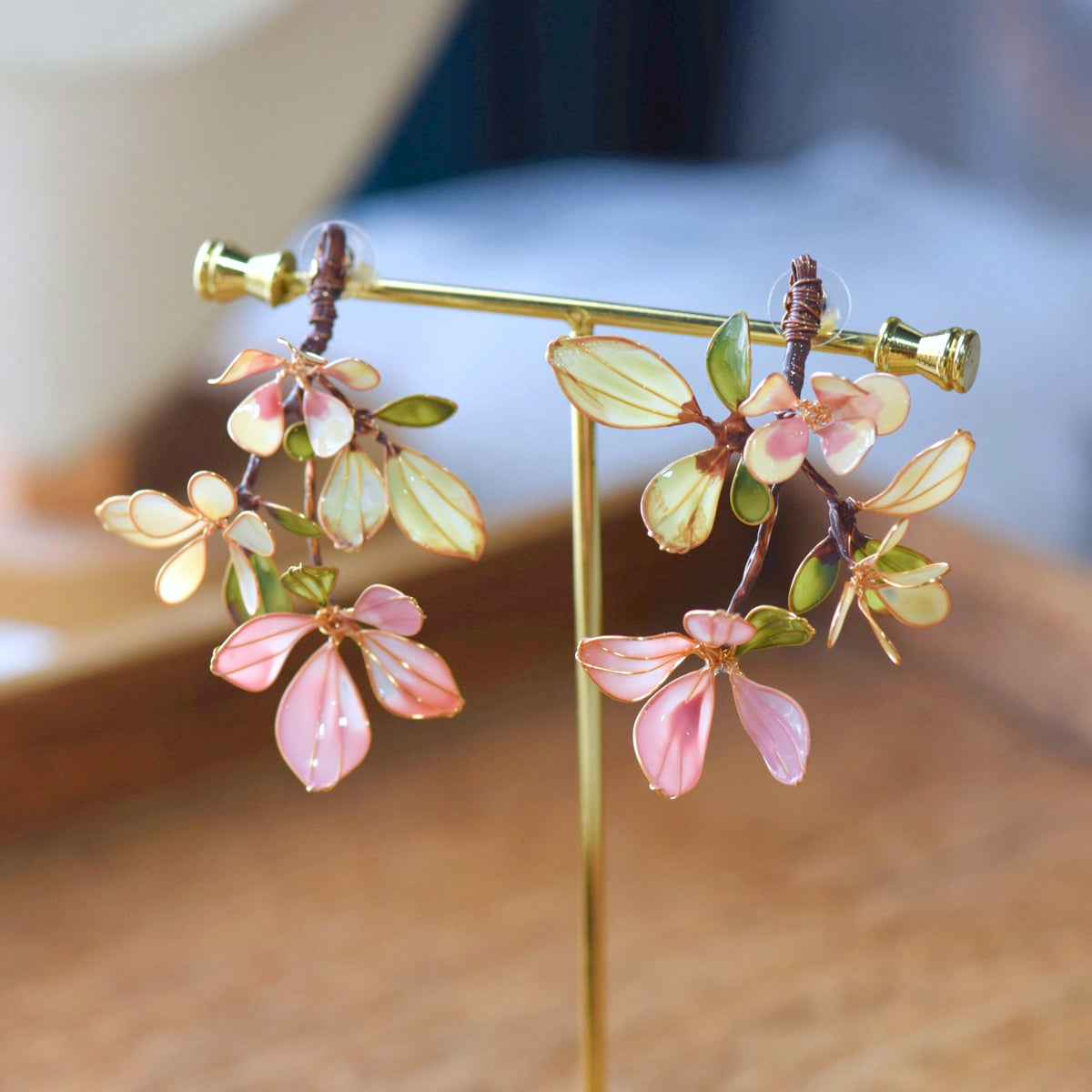 Aveline pink and green resin floral branch earrings with gold veining on a display stand
