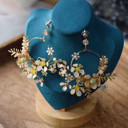 Betty yellow beige and gold resin floral long drop earrings on a navy display stand
