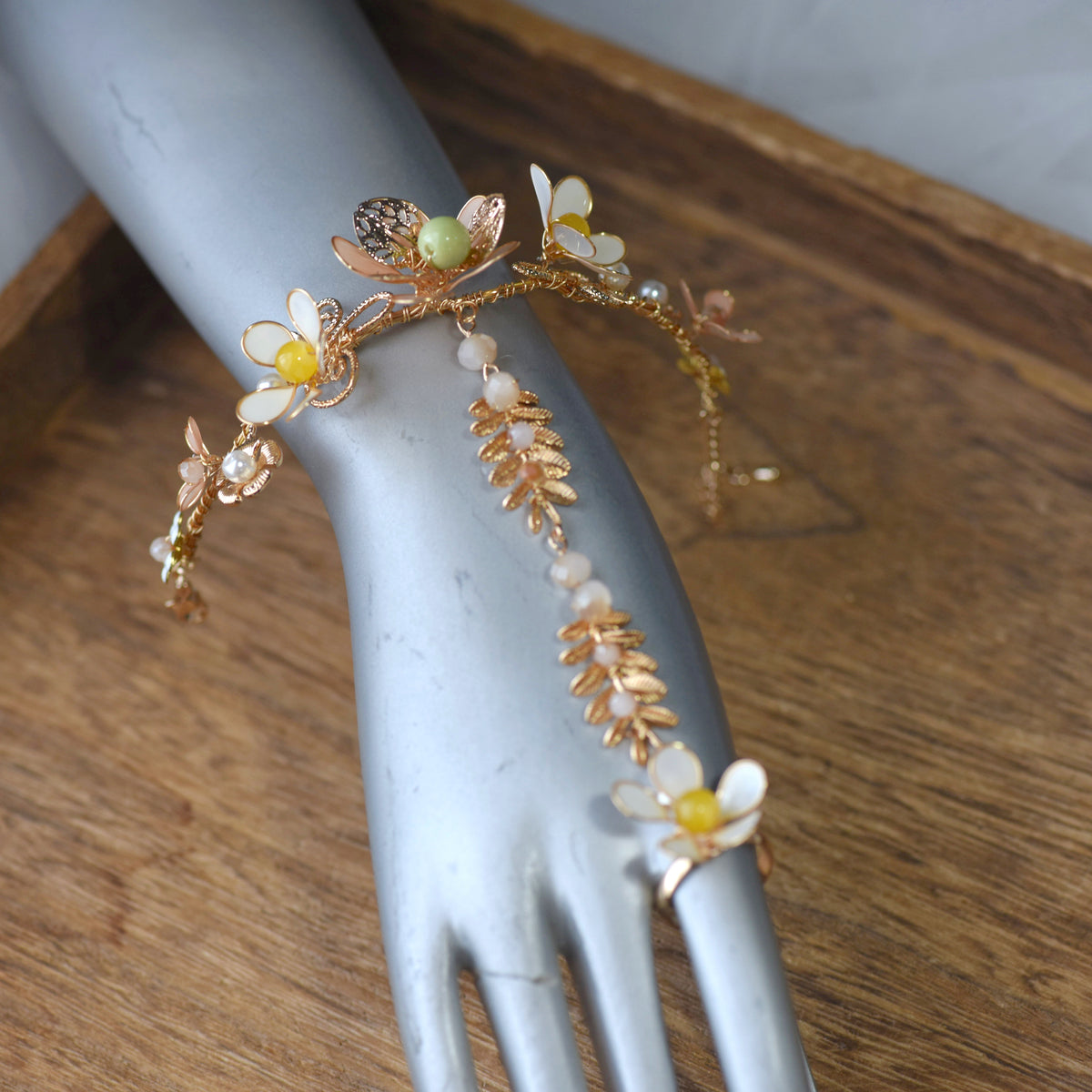 Betty yellow gold and green resin floral haath phool shown on a mannequin hand with adjustable ring and bracelet
