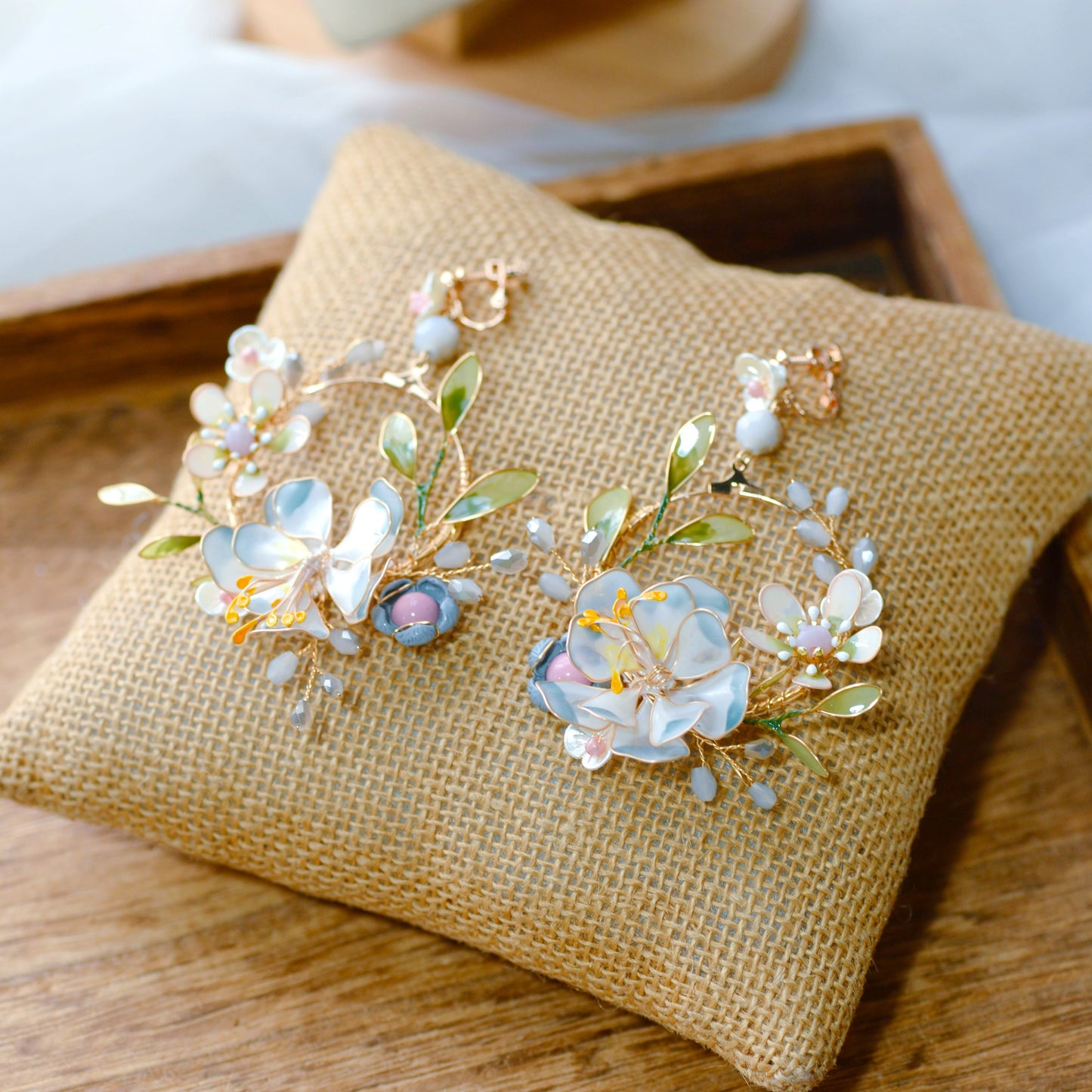 Bluesette handcrafted blue green white resin floral drop earrings flat lay burlap cushion botanical statement
