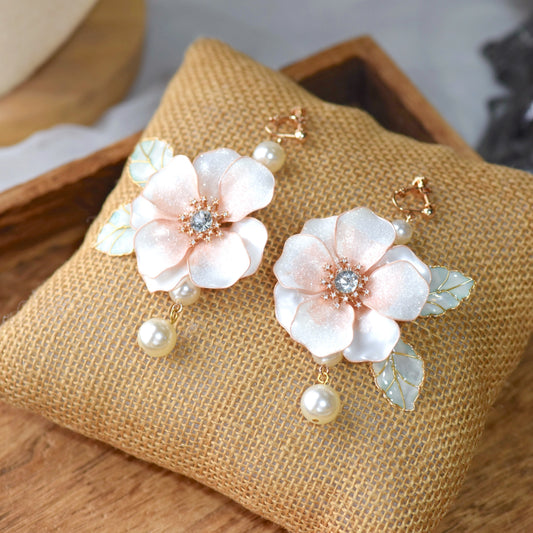 Camellias white and blush resin floral drop earrings with pearls and mother of pearl leaves on a jute cushion
