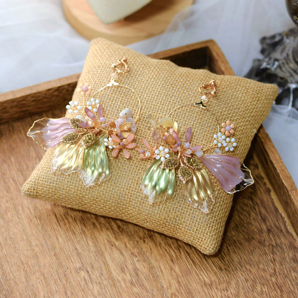 Catriona lavender and green resin floral earrings with golden wirework laid on a jute cushion
