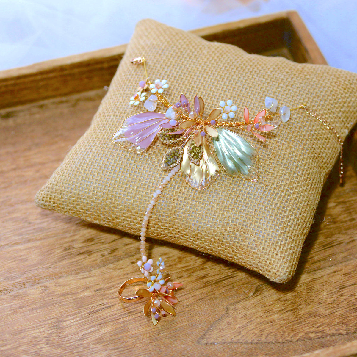 Catriona pastel resin floral hand harness in pink, lavender and mint laid on a jute cushion
