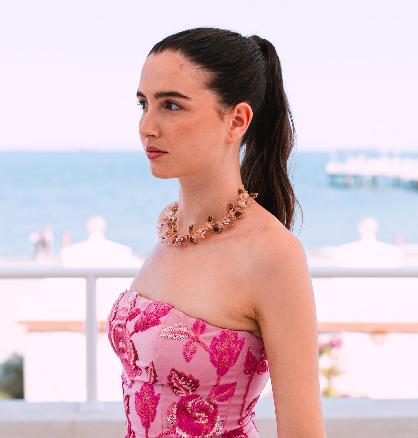 Model wearing Celestina handcrafted resin floral necklace pink gold with pink dress outdoor
