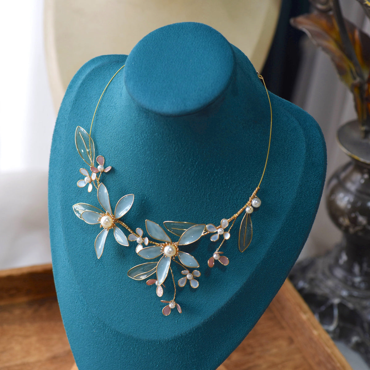 Cerulean pastel blue resin floral necklace with pearls displayed on a teal bust
