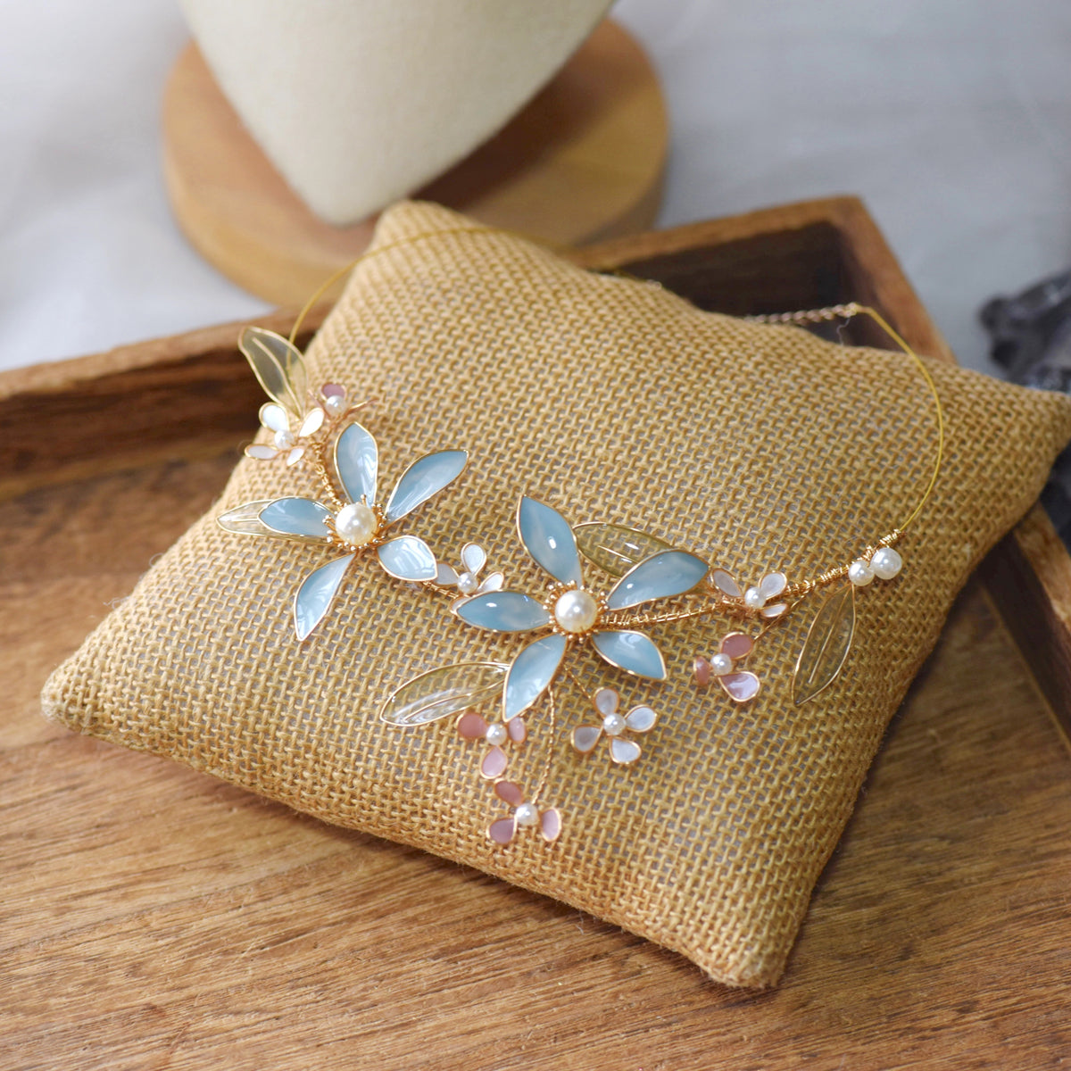 Cerulean pastel blue and green resin floral necklace with pearl clusters on a jute cushion
