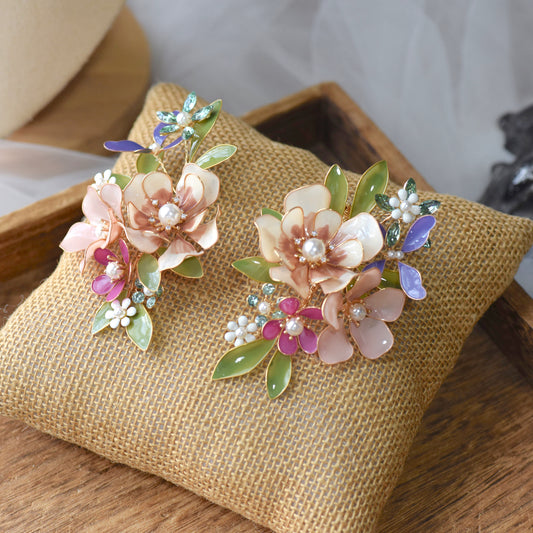 Chloe blush and mauve resin floral earrings with pearl centres laid on a jute cushion
