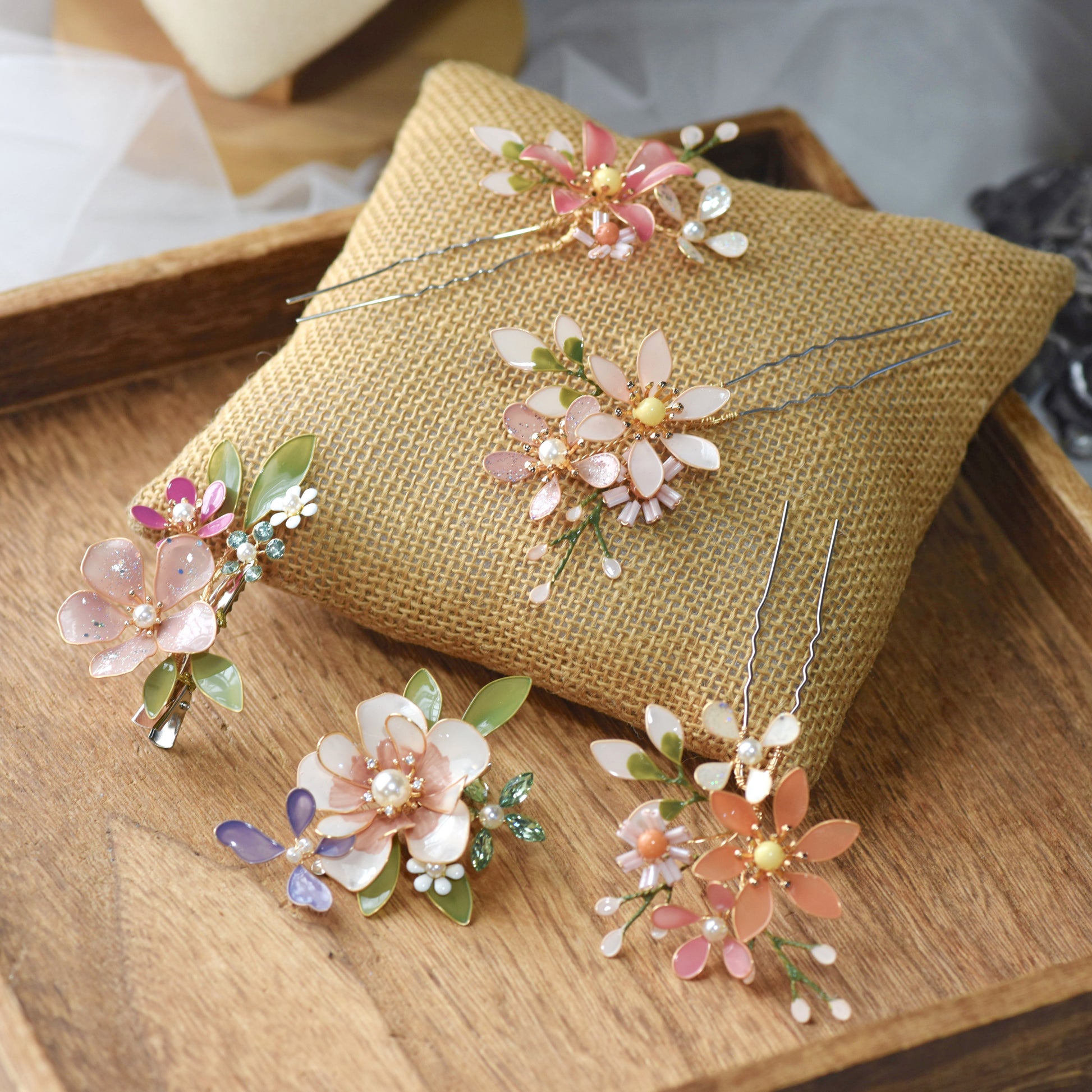 Chloe set of five blush and mauve resin floral hair pins with pearl centres on a jute cushion
