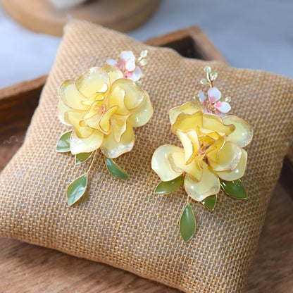 Elena butter yellow resin floral rose earrings with green leaf drops on a jute cushion