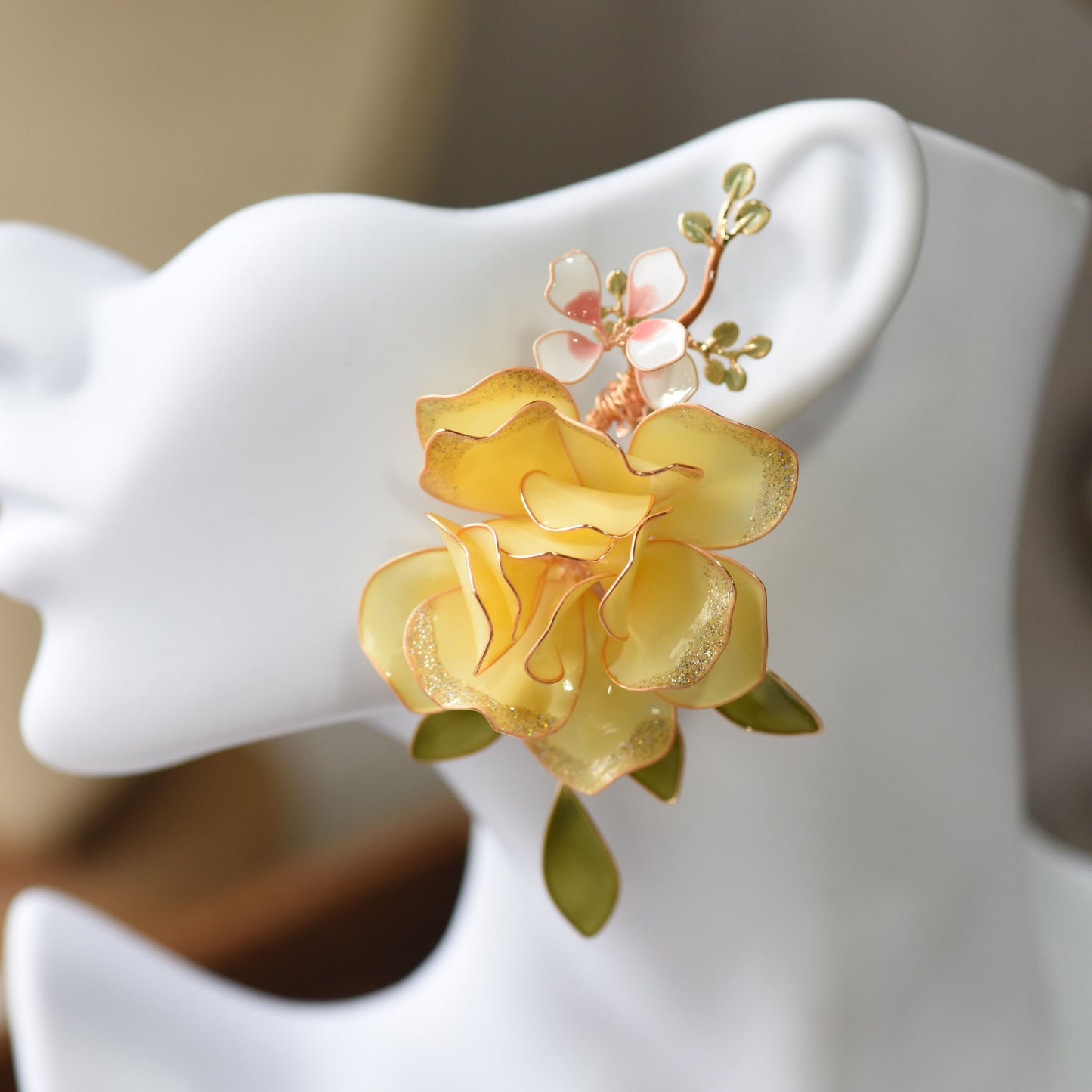 Elena butter yellow resin floral rose earrings shown on a white ear display