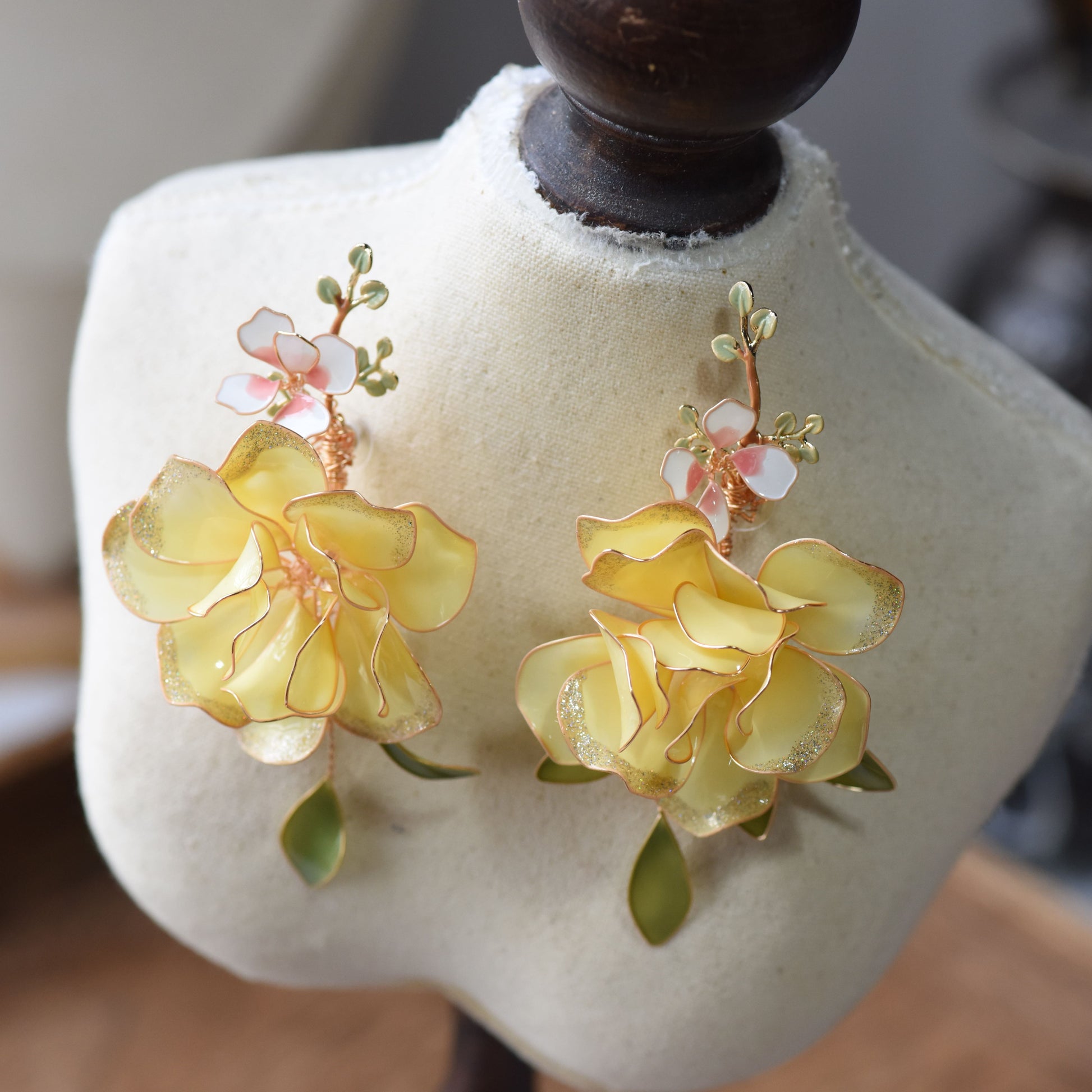 Elena butter yellow and green resin floral statement earrings on a white display bust