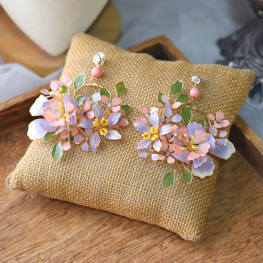 Ella blush pink and lavender resin floral statement earrings with sage leaves on a jute cushion
