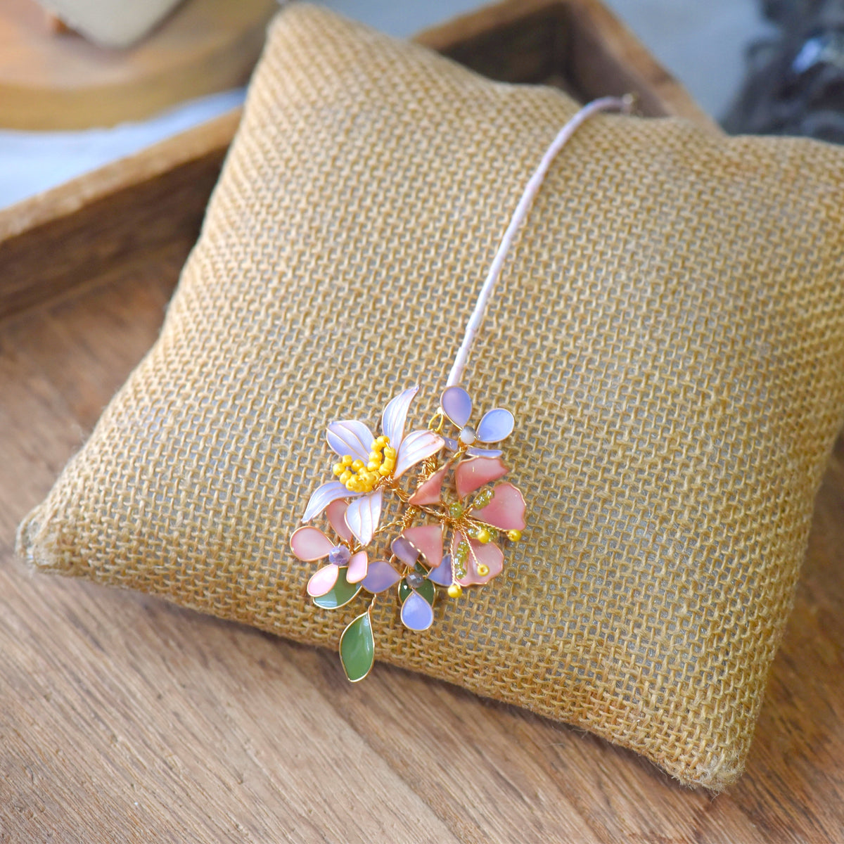 Ella blush pink and lavender resin floral bridal maang tika with sage leaf drop on a jute cushion