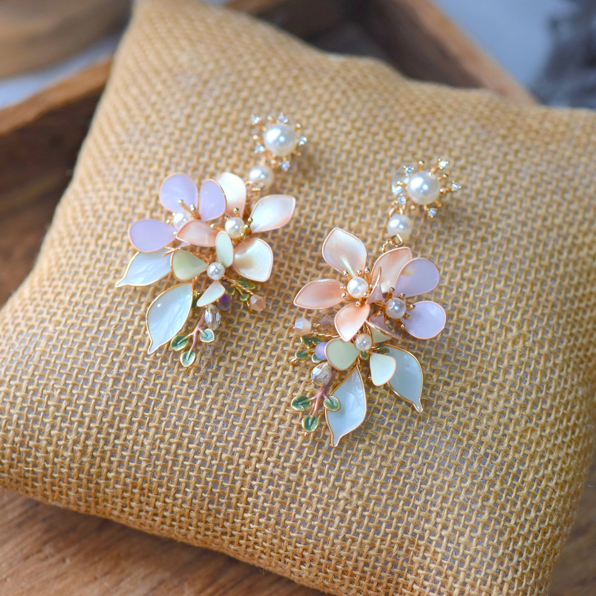 Elowen blush, ivory and mint resin floral earrings with pearls laid on a jute cushion
