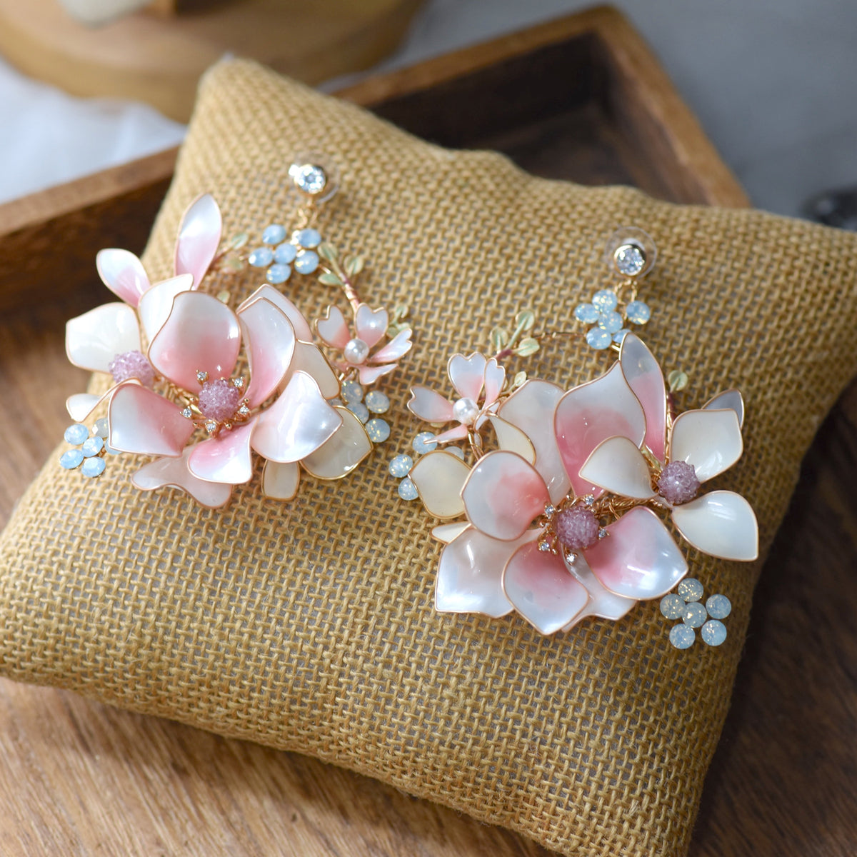 Elvyne white resin floral earrings with soft pink centres laid on a jute cushion
