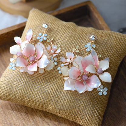 Elvyne white resin floral earrings with soft pink centres laid on a jute cushion
