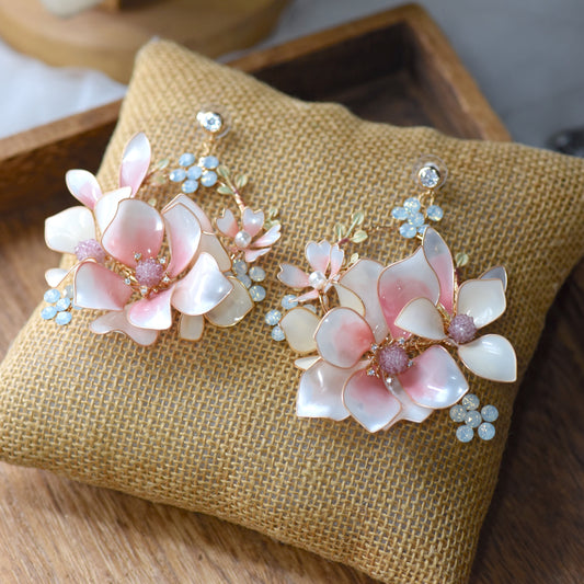 Elvyne white resin floral earrings with soft pink centres laid on a jute cushion
