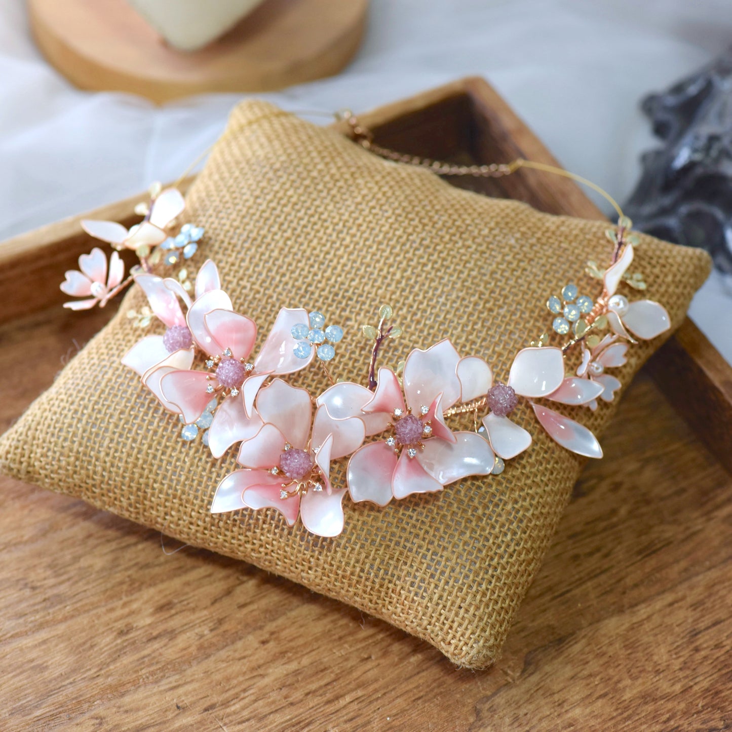 Elvyne white resin floral necklace with soft pink centres laid on a jute cushion

