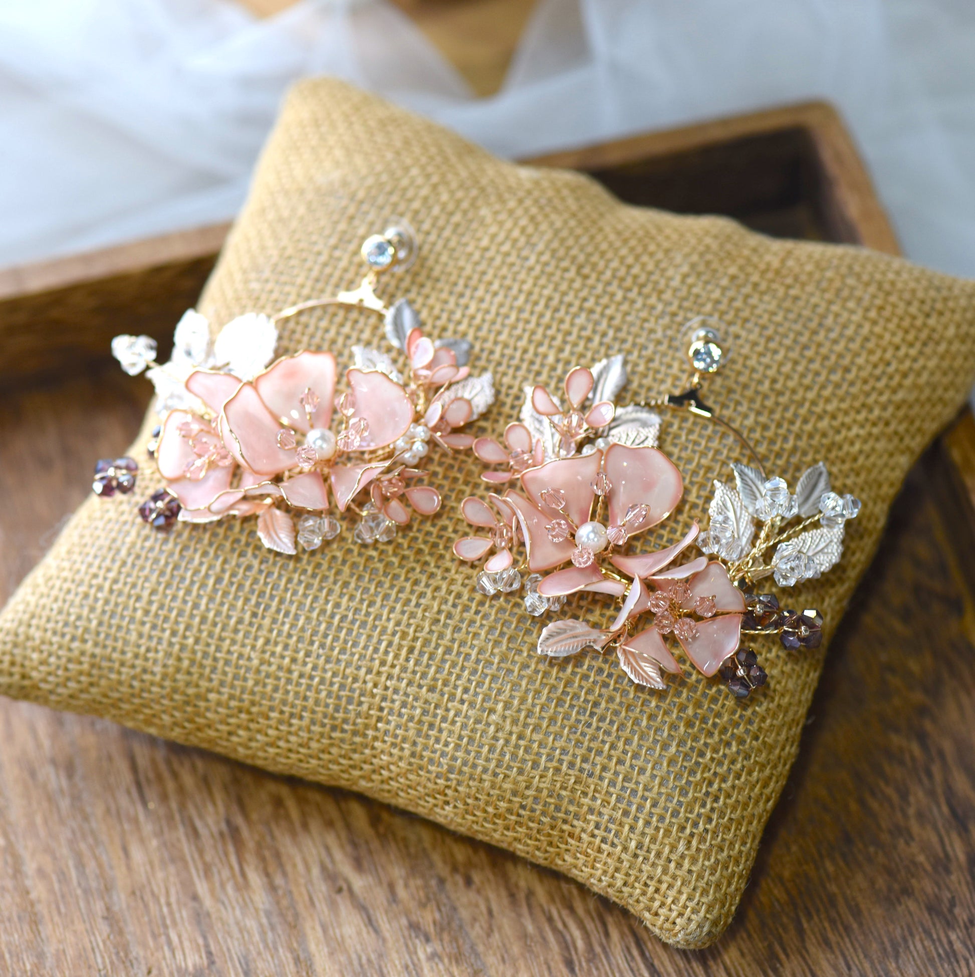 Eos blush pink resin floral earrings laid on a jute cushion
