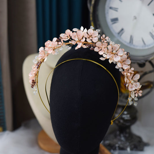 Eos blush pink resin floral crown headband with golden and purple bead accents on a display stand
