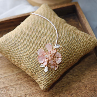 Eos blush pink resin floral maang tika with delicate chain laid on a jute cushion
