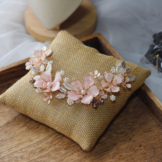 Eos blush pink resin floral necklace with golden and purple bead accents laid on a jute cushion

