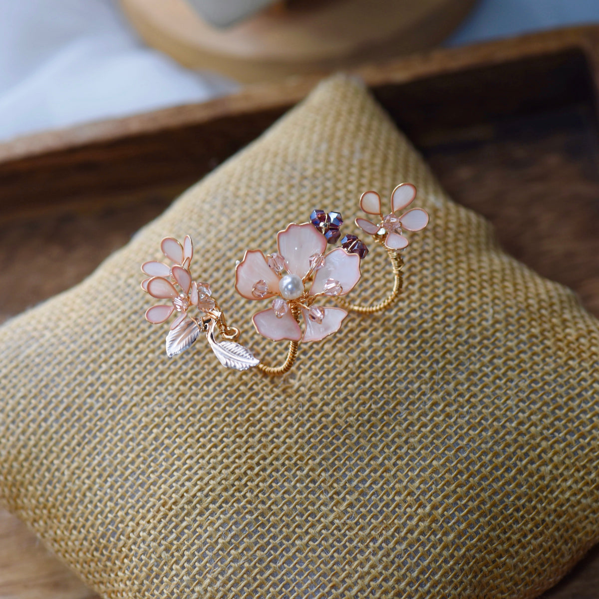Eos blush pink resin floral statement ring with purple bead accents on a jute cushion
