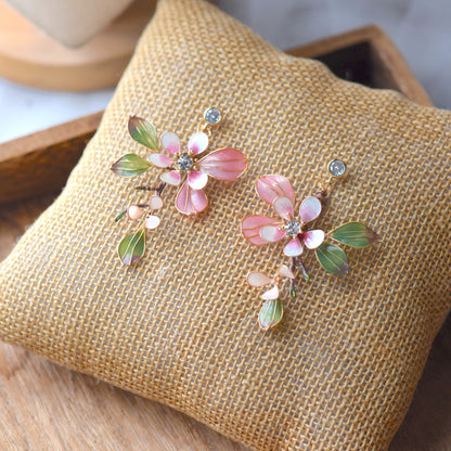 Florentine blush pink resin floral earrings with olive green leaves and zirconia centres on a jute cushion
