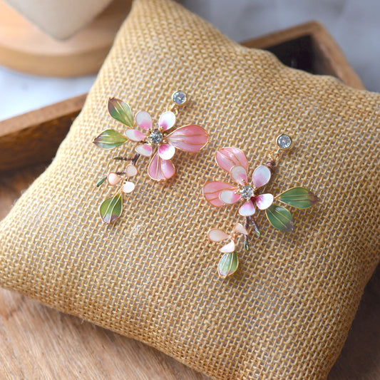 Florentine blush pink resin floral earrings with olive green leaves and zirconia centres on a jute cushion
