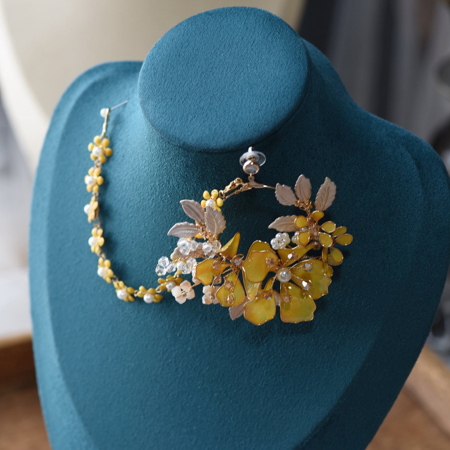 Helios earrings with hair harness on display stand showing yellow blooms and golden wirework detail
