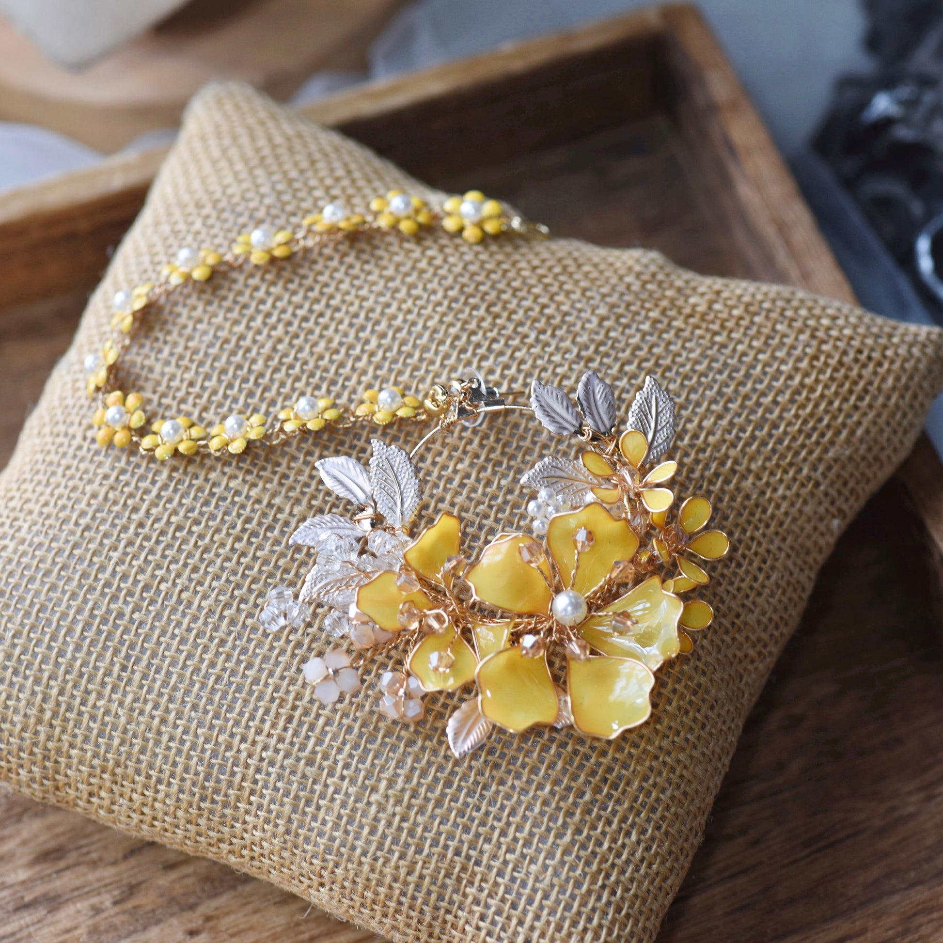 Helios yellow resin floral earrings with trailing hair harness laid on a jute cushion
