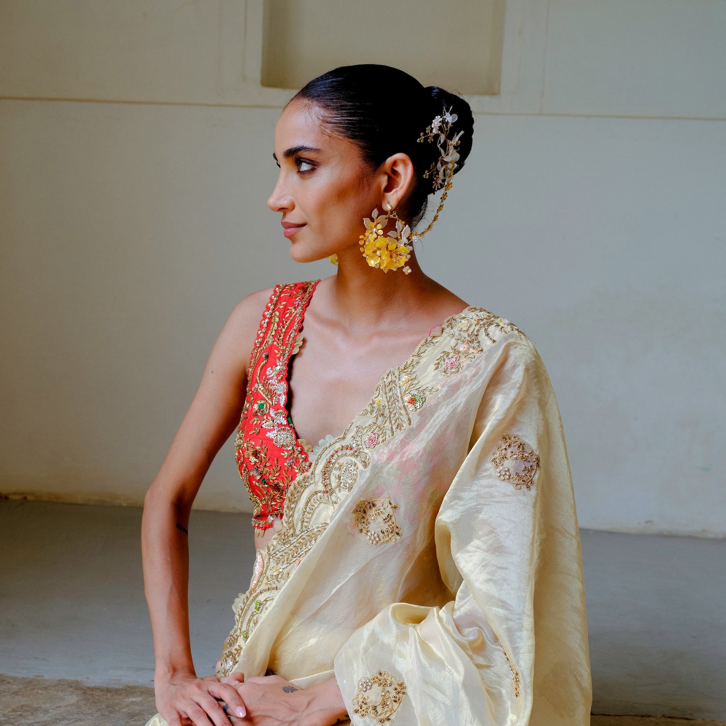 Model seated wearing Helios yellow floral earrings with hair harness in a festive look
