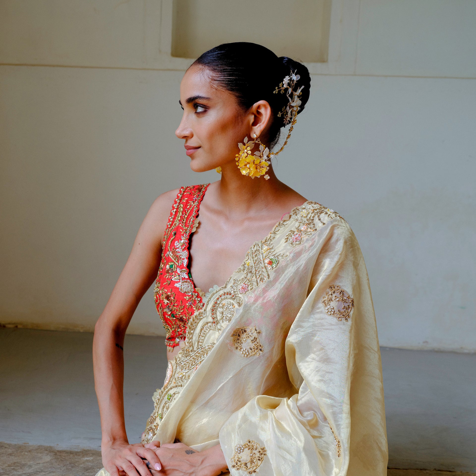 Model seated wearing Helios yellow floral earrings with hair harness in a festive look
